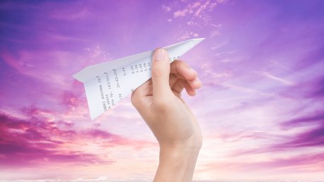 Käsi pitelemässä kuitista tehtyä paperilennokkia